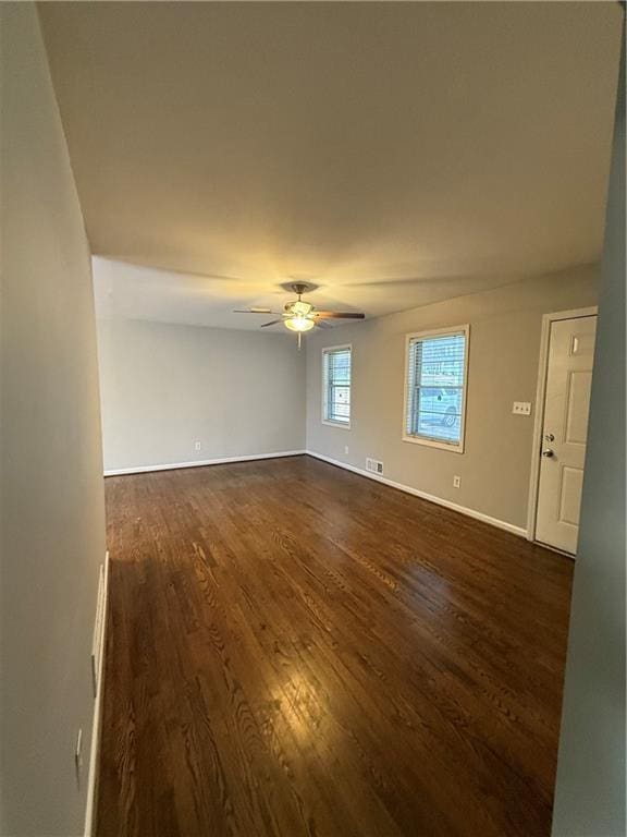 empty room featuring dark wood-style floors, visible vents, ceiling fan, and baseboards
