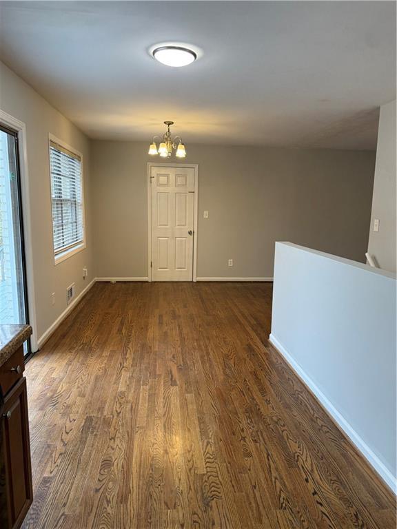 empty room with an inviting chandelier, baseboards, dark wood-type flooring, and visible vents