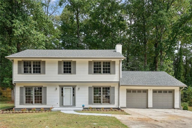 colonial-style house featuring a garage, driveway, roof with shingles, a chimney, and a front yard