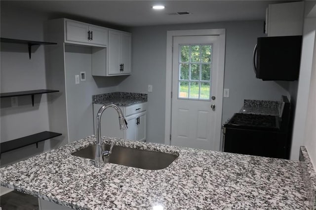 kitchen with white cabinetry, stove, sink, and light stone counters