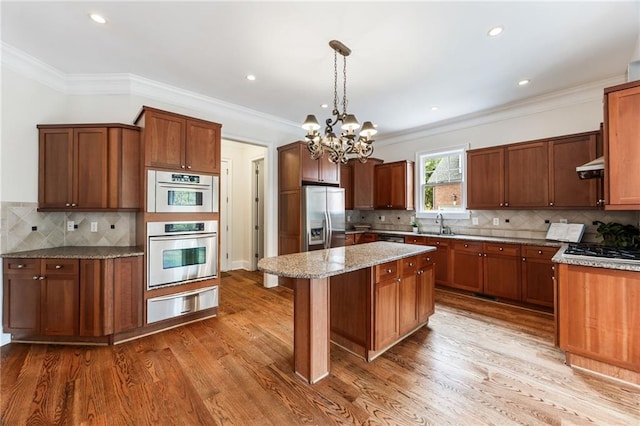 kitchen featuring a center island, hanging light fixtures, appliances with stainless steel finishes, light stone counters, and a chandelier