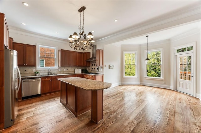 kitchen with appliances with stainless steel finishes, a center island, decorative light fixtures, and wall chimney exhaust hood