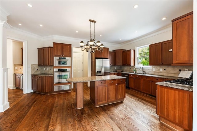 kitchen with pendant lighting, dark wood-type flooring, crown molding, appliances with stainless steel finishes, and a kitchen island