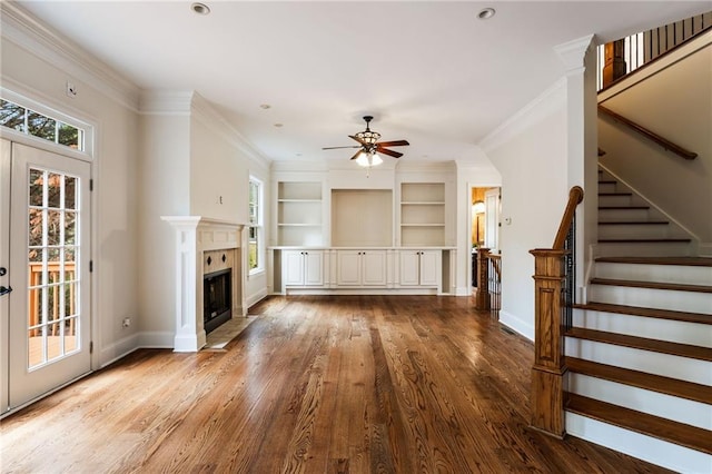 unfurnished living room featuring ceiling fan, crown molding, wood-type flooring, built in features, and a fireplace