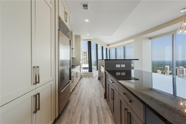 kitchen featuring light hardwood / wood-style floors, stainless steel built in fridge, hanging light fixtures, and dark stone counters