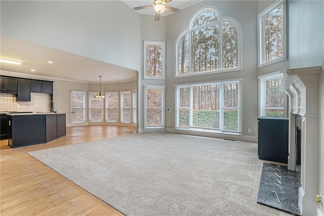 unfurnished living room with light carpet, ornamental molding, a high ceiling, a fireplace, and ceiling fan