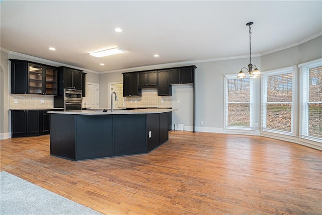 kitchen with light wood-style flooring, ornamental molding, backsplash, light countertops, and a chandelier