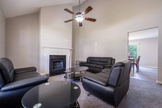 carpeted living area featuring ceiling fan, a fireplace, baseboards, and high vaulted ceiling