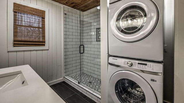 clothes washing area featuring laundry area, a sink, stacked washer / drying machine, wooden ceiling, and dark tile patterned floors