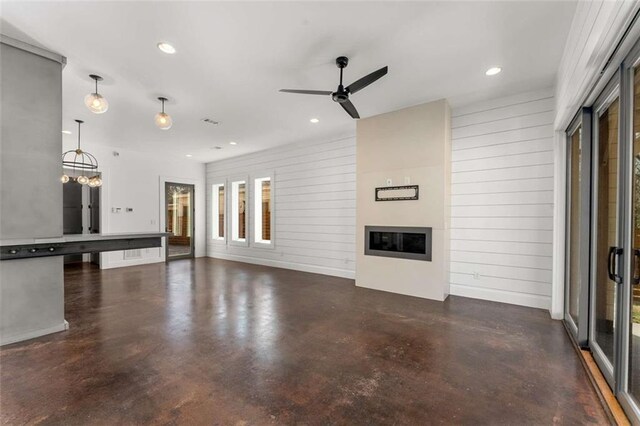 unfurnished living room with visible vents, finished concrete flooring, recessed lighting, ceiling fan with notable chandelier, and a glass covered fireplace