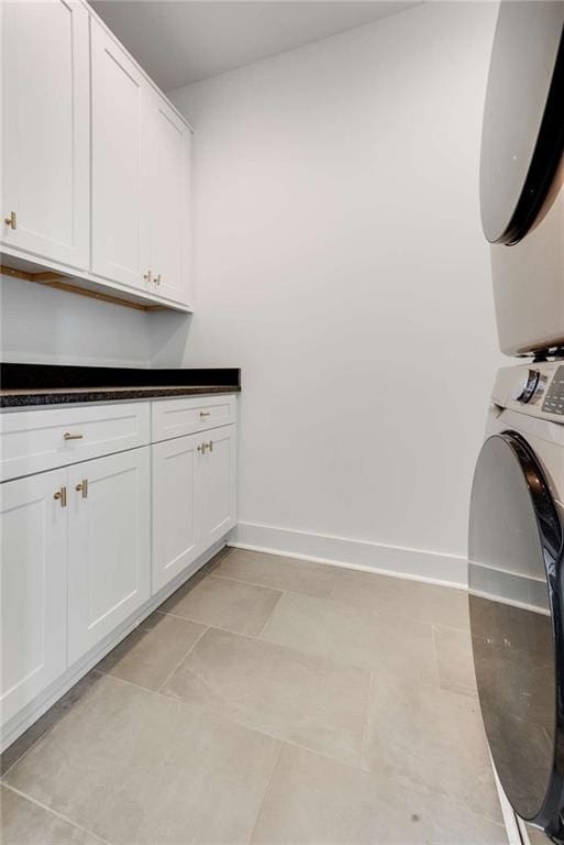 washroom with cabinet space, stacked washer / drying machine, and baseboards