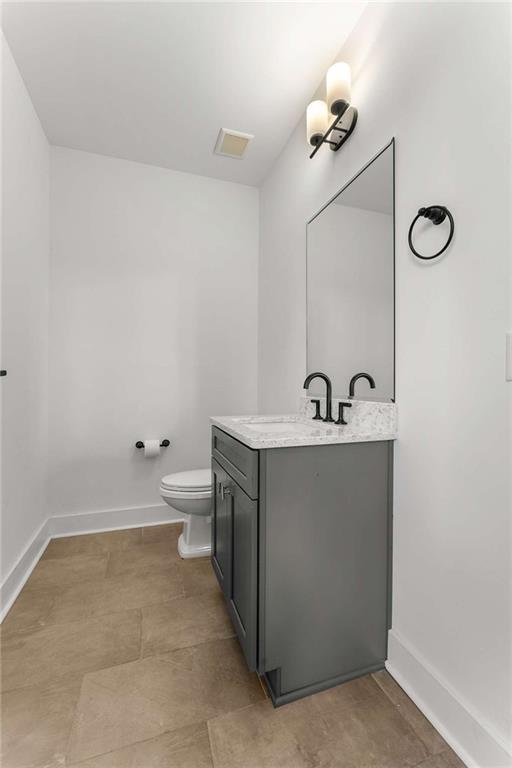 half bathroom featuring visible vents, toilet, vanity, and baseboards