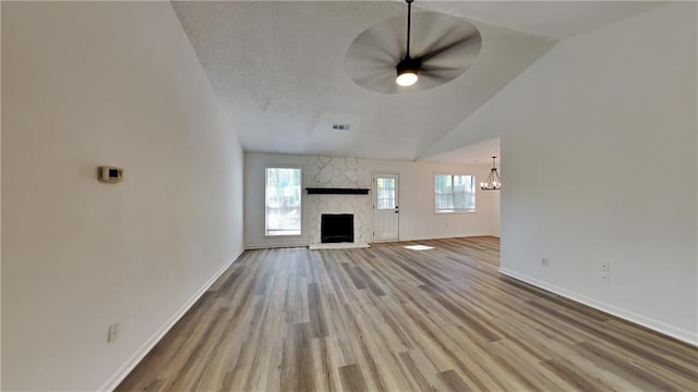 unfurnished living room with light wood-type flooring, ceiling fan with notable chandelier, a stone fireplace, and lofted ceiling