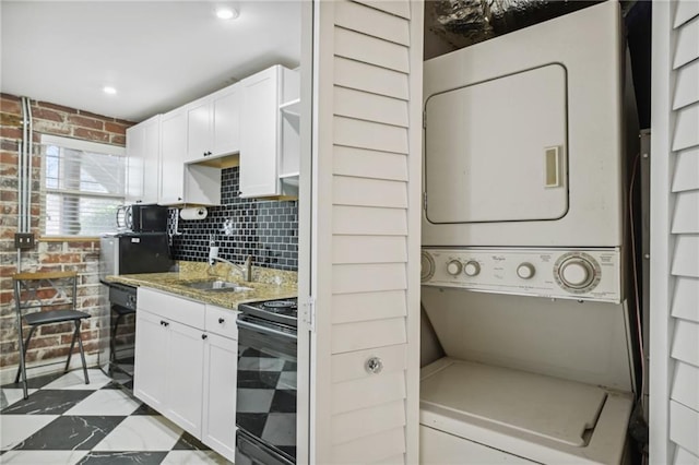 kitchen with black electric range oven, white cabinetry, brick wall, stacked washing maching and dryer, and beverage cooler