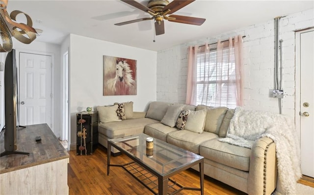 living area featuring brick wall, wood finished floors, and a ceiling fan