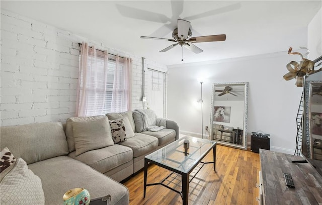 living room with baseboards, crown molding, light wood finished floors, and brick wall