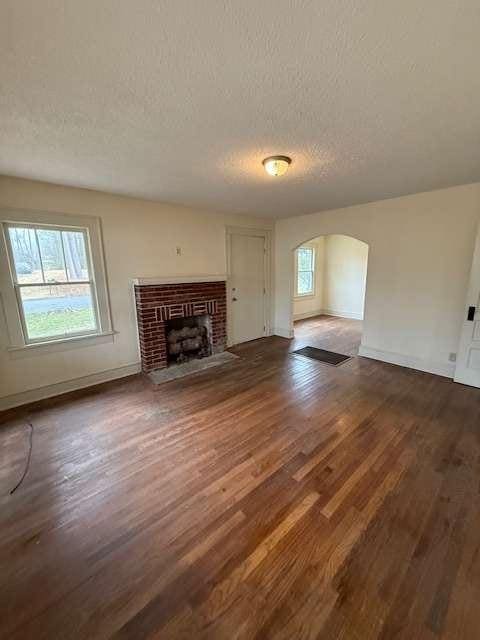 unfurnished living room with a brick fireplace, dark wood-type flooring, and a textured ceiling