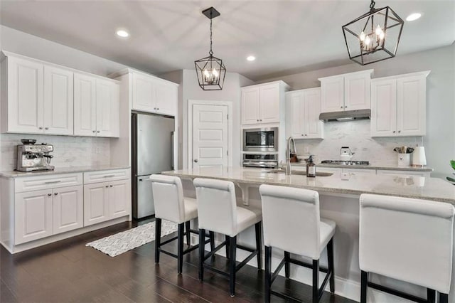 kitchen featuring white cabinetry, stainless steel appliances, an island with sink, and pendant lighting