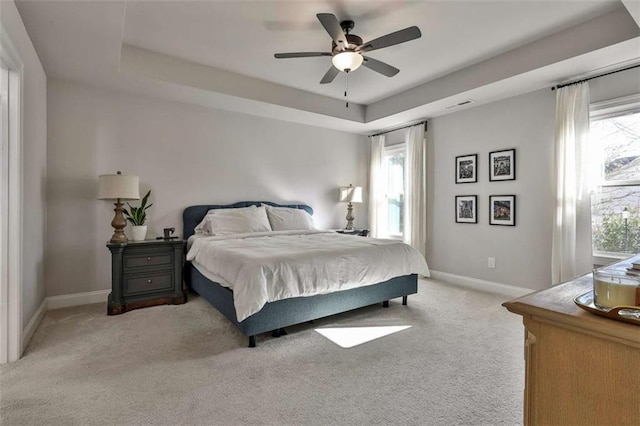 bedroom with light colored carpet, ceiling fan, and a tray ceiling