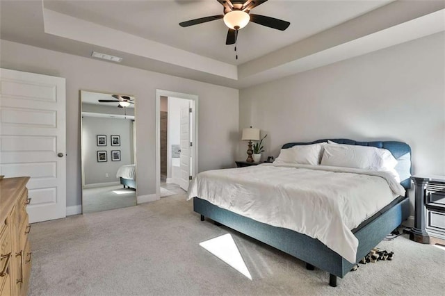 bedroom with ceiling fan, ensuite bathroom, a raised ceiling, and light carpet