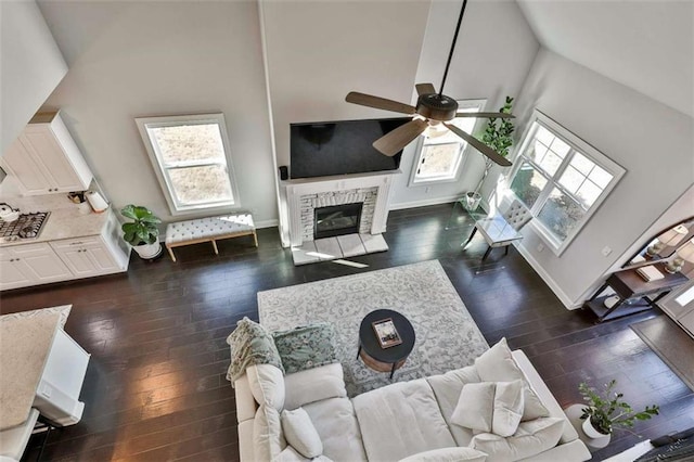 living room featuring dark hardwood / wood-style floors, ceiling fan, a stone fireplace, and high vaulted ceiling