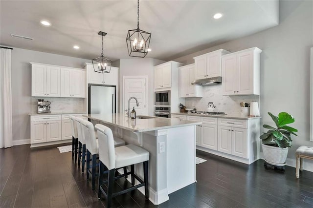 kitchen featuring appliances with stainless steel finishes, decorative light fixtures, white cabinetry, an island with sink, and sink