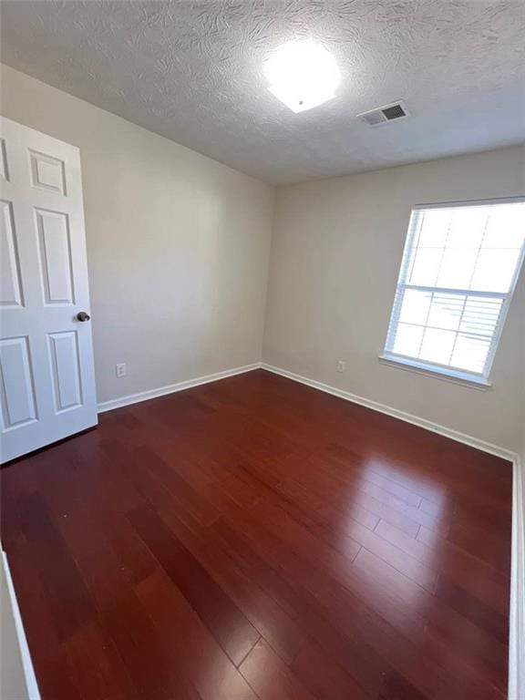 spare room with dark hardwood / wood-style floors and a textured ceiling