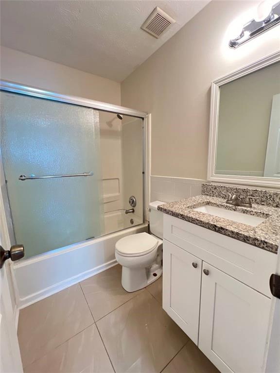 full bathroom featuring shower / bath combination with glass door, tile patterned floors, vanity, and toilet