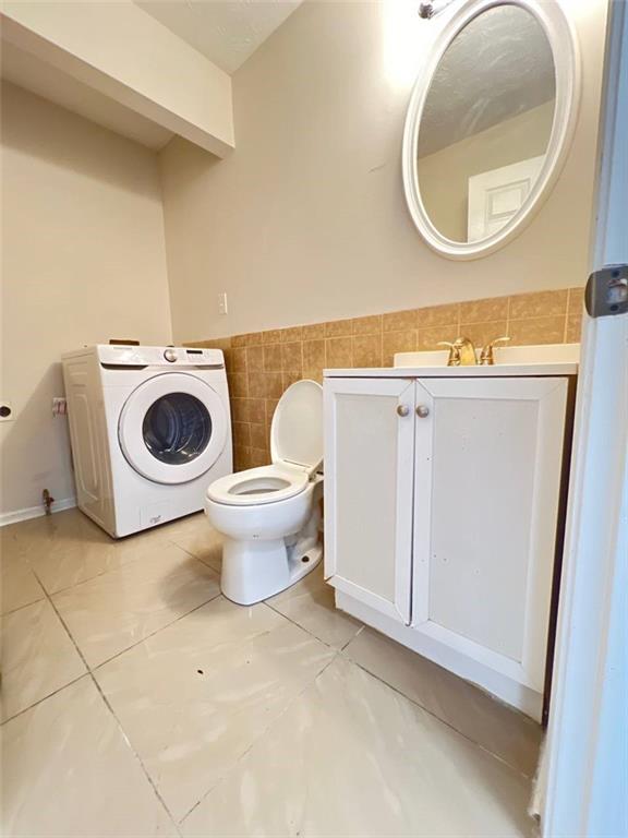 bathroom featuring washer / clothes dryer, vanity, tile walls, and toilet