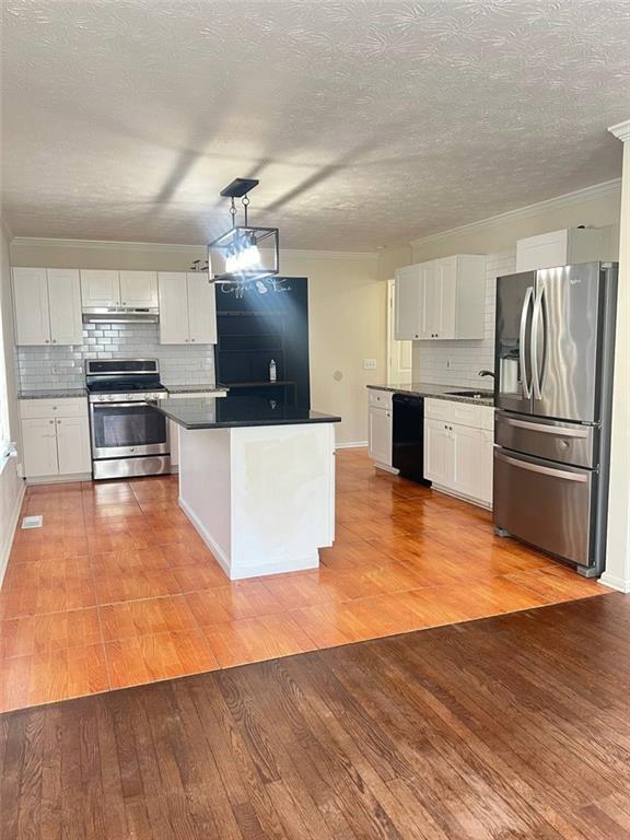 kitchen with pendant lighting, stainless steel appliances, white cabinetry, and light hardwood / wood-style floors