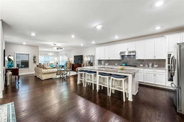 kitchen with a center island with sink, stainless steel fridge, light stone counters, white cabinets, and a kitchen breakfast bar