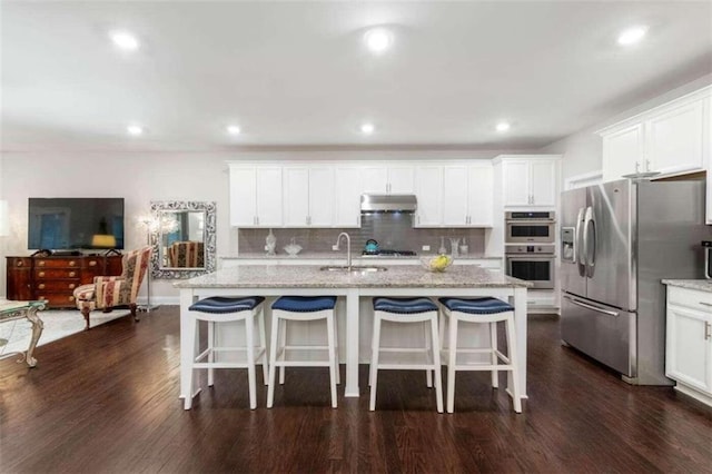 kitchen with a center island with sink, appliances with stainless steel finishes, white cabinetry, and light stone countertops