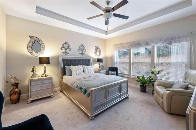 bedroom featuring a raised ceiling, light carpet, and ceiling fan