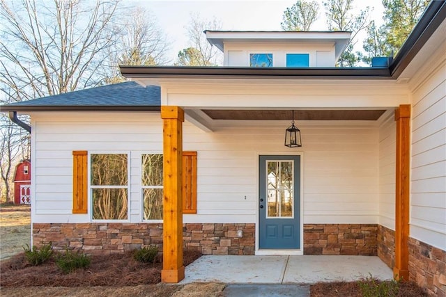 entrance to property with stone siding, a shingled roof, and a porch