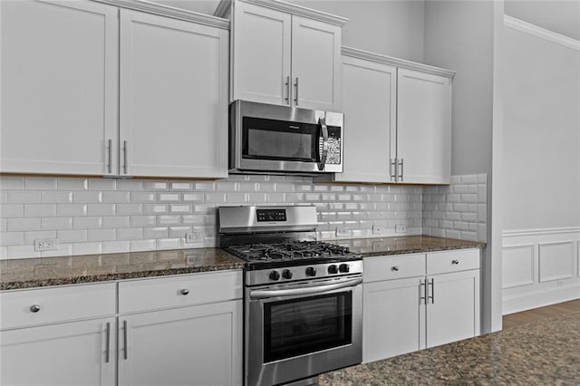6469 Crosscreek Ln, Flowery Branch, GA 30542 - kitchen with stainless steel appliances, dark stone countertops, crown molding, white cabinetry, and wainscoting