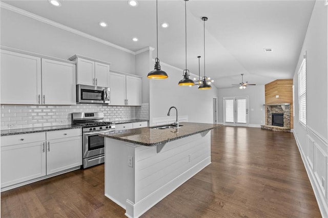 6469 Crosscreek Ln, Flowery Branch, GA 30542 - kitchen featuring appliances with stainless steel finishes, ceiling fan, a stone fireplace, dark stone countertops, and a center island with sink