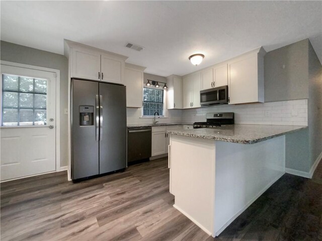 kitchen featuring stainless steel appliances, white cabinets, hardwood / wood-style flooring, and backsplash