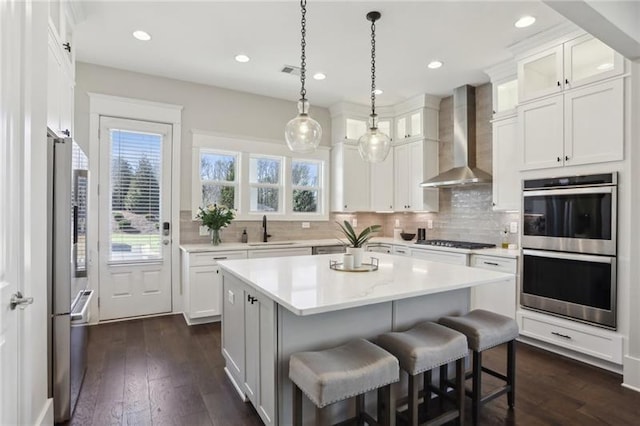 kitchen with a center island, light countertops, white cabinets, stainless steel appliances, and wall chimney exhaust hood
