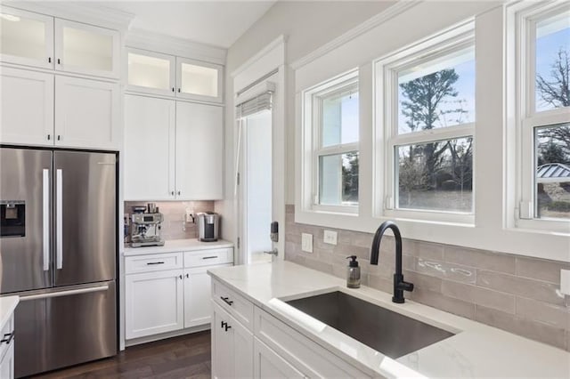 kitchen with stainless steel refrigerator with ice dispenser, a sink, decorative backsplash, and white cabinetry
