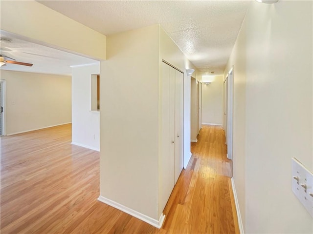 corridor with a textured ceiling and light hardwood / wood-style flooring