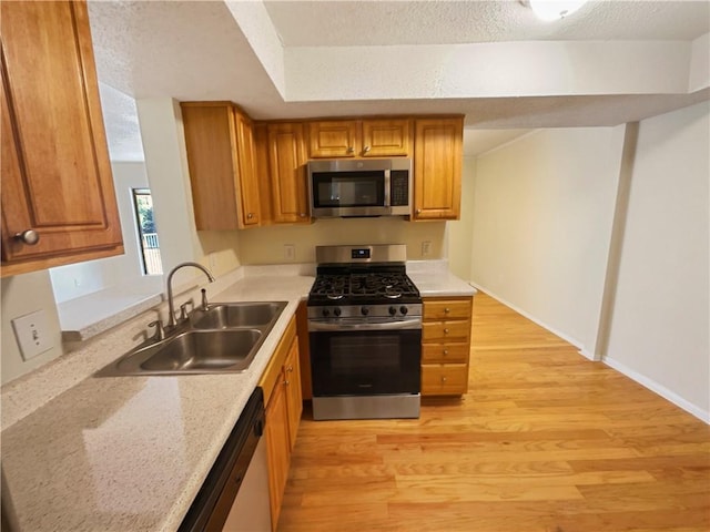 kitchen with appliances with stainless steel finishes, a textured ceiling, a raised ceiling, sink, and light hardwood / wood-style floors