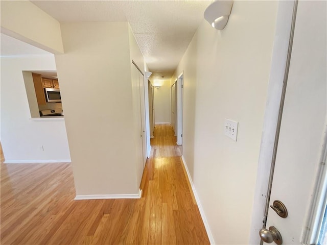 hallway with light hardwood / wood-style flooring and a textured ceiling