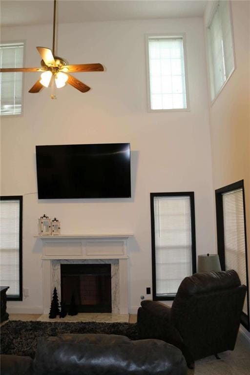 living room featuring a premium fireplace, a towering ceiling, and ceiling fan