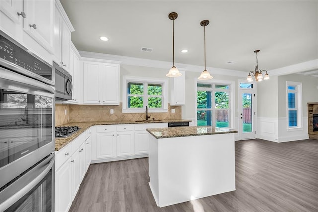 kitchen featuring stainless steel appliances, decorative light fixtures, sink, white cabinets, and hardwood / wood-style flooring