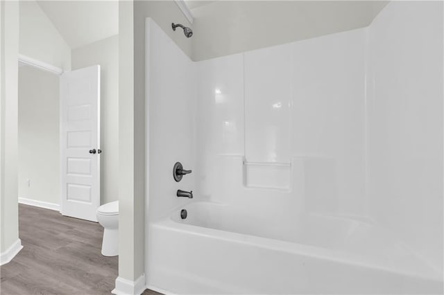 bathroom featuring vaulted ceiling, toilet, hardwood / wood-style flooring, and shower / washtub combination