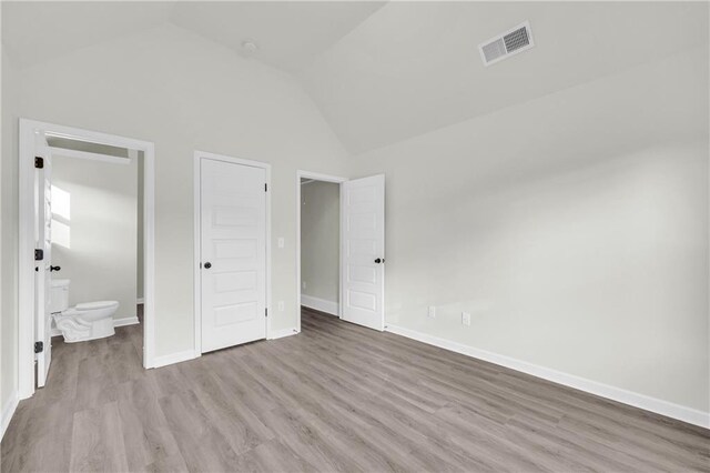 unfurnished bedroom featuring high vaulted ceiling, ensuite bathroom, and wood-type flooring