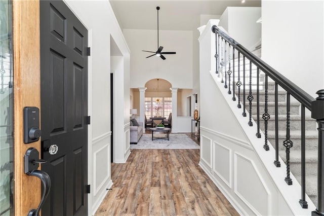 entrance foyer with a towering ceiling, hardwood / wood-style floors, ceiling fan, and decorative columns