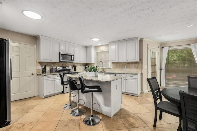 kitchen with white cabinetry, stainless steel appliances, a kitchen island, light stone countertops, and a breakfast bar area