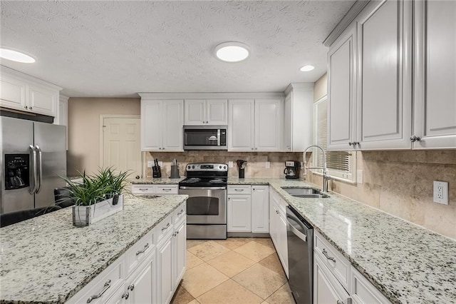 kitchen featuring white cabinets, backsplash, light stone countertops, stainless steel appliances, and sink