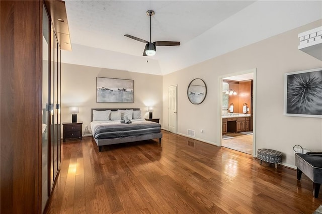 bedroom with ceiling fan, connected bathroom, wood-type flooring, and vaulted ceiling